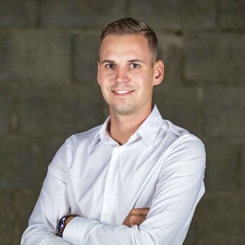 Portrait zeigt Mathias Kölbl die Arme verschränkend vor dunklem Hintergrund.